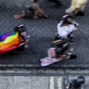 reizen als LHBTQIA+: in deze foto zie je een persoon met een regenboogvlag omgeknoopt op straat lopen.