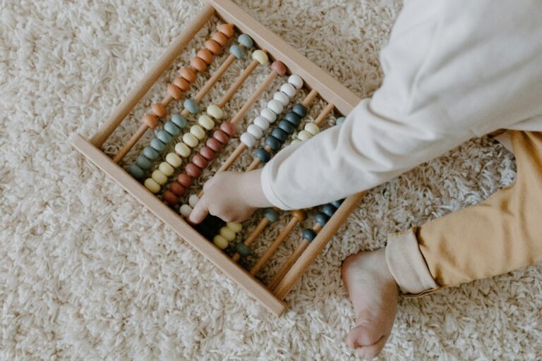 Op de foto speelt een baby met een houten kraalrek. Je kunt het gezicht van de baby niet zien.