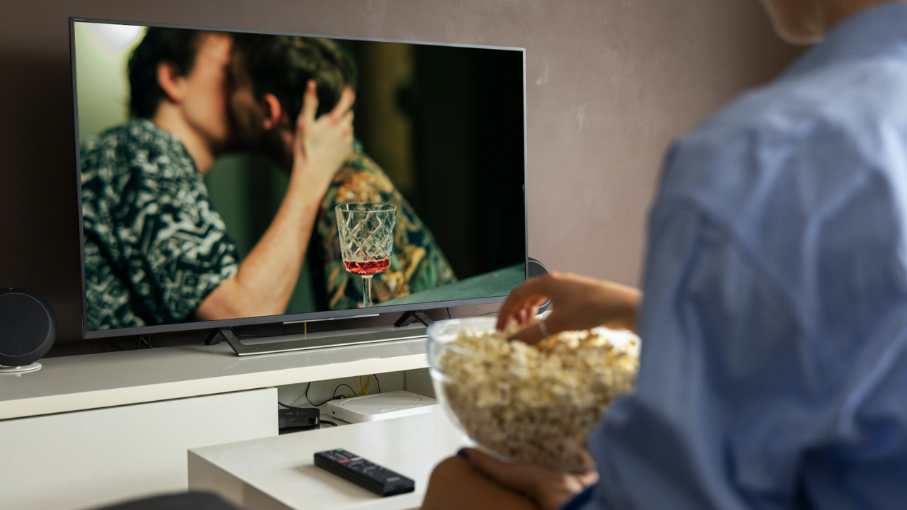 Vrouw kijkt naar een televisie waarop twee mannen aan het zoenen zijn.